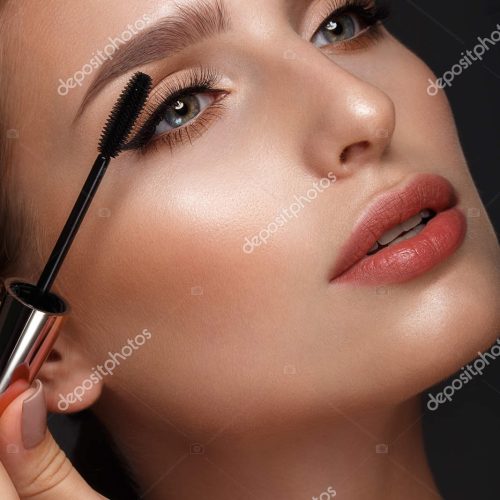 Beautiful girl with sexy lips and classic makeup with cosmetic mascara brush in hand. Beauty face. Photo taken in the studio.